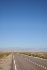 A straight road goes into the horizon at the Chisos Mountains at Big Bend National Park in Texas with the moon visable.