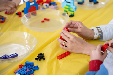 Female hands of a mother helping her child putting together the building blocks during the birthday party