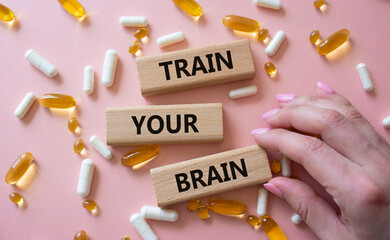 Train Your Brain symbol. Concept words Train Your Brain on wooden blocks. Beautiful pink background with pills. Doctor hand. Healthcare and Train Your Brain concept. Copy space.