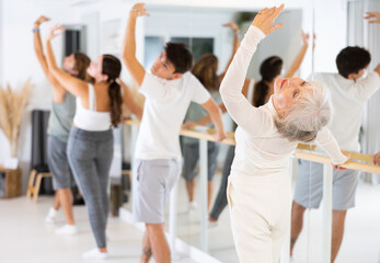 Group of people of different ages practice ballet moves in classical dance school.