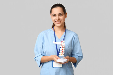 Portrait of female doctor with spine model on grey background