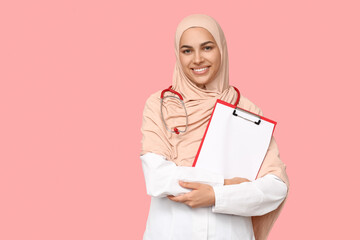 Portrait of female Muslim doctor holding clipboard with blank paper sheet on pink background