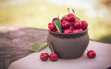 Cherries in ceramic bowl. Red cherry and leaf in cup on wooden background on sunlight. Fresh...