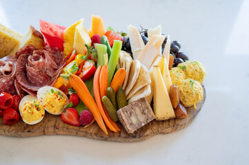 Gourmet charcuterie grazing board with fresh vegetables, meats, and cheeses arranged on a wooden platter white marble table