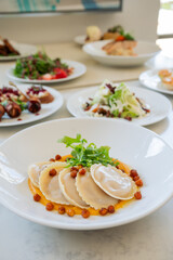 A white plate with round ravioli. The plate is set on a table with other plates of food in the background.