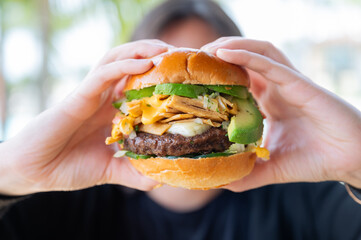 Hands holding a juicy gourmet hamburger in front of face. Color photo 