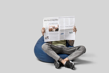 Man in beanbag chair with newspaper on grey background