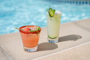 Strawberry Watermelon cocktail margarita and mint mojito next to the edge of a blue pool  