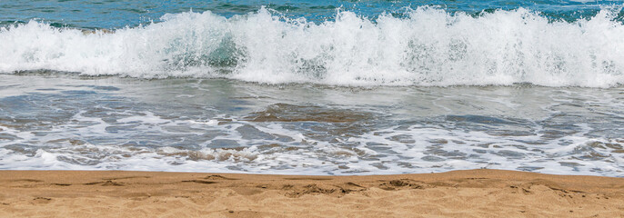 Blue and turquoise colored sea waves with white foam and yellow sand. Sea beach background, summer banner. Sea background with sand on a sunny day