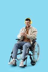 Happy young man in wheelchair with headphones using mobile phone on blue background