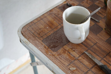 A camping table that is a bit dirty. There is a mug on it.