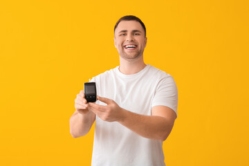 Handsome young happy diabetic man with glucometer on yellow background