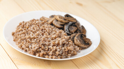 Buckwheat porridge with fried mushrooms on a plate on a wooden background. Healthy diet food. The concept of healthy eating