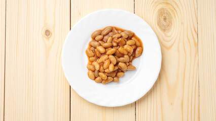 baked beans in sauce on a white plate close-up on a wooden background. the view from the top.