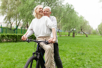 Obraz premium elderly senior couple rides bicycle in the park in the summer and smiles, old gray-haired man and woman are actively resting outdoors, old people practice cycling in forest