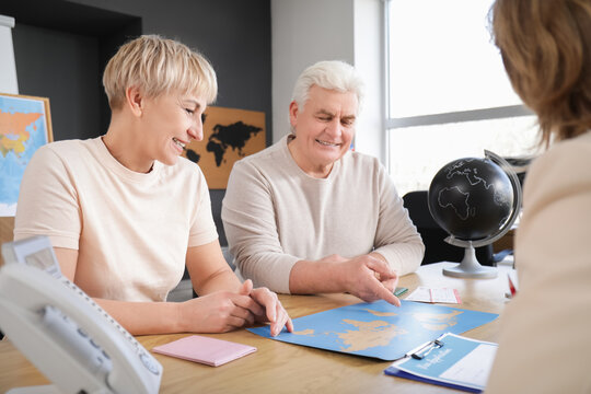 Happy mature couple with world map planning trip in travel agency