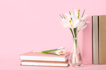 Glass vase with beautiful white crocus flowers and books on pink background