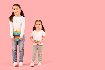 Cute little Asian happy sisters with different pop it fidget toys on pink background