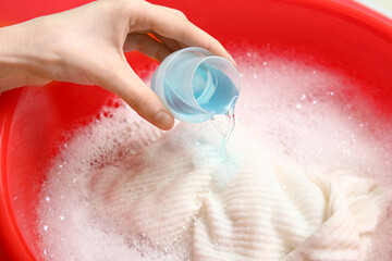 Fototapeta premium Woman adding laundry detergent to clothes in plastic basin, closeup