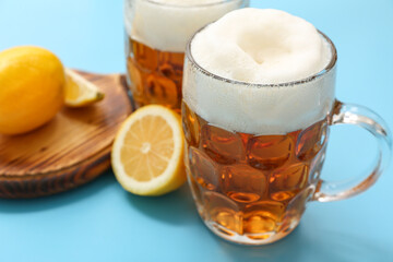 Glasses of fresh beer and wooden board with lemon on blue background