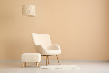 Comfortable armchair, pouf and lamp near beige wall