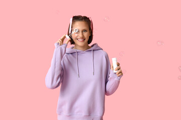 Happy teenage girl blowing soap bubbles on pink background