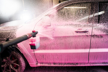 Spraying pink foam detergent on the car at a self service car wash. The process of applying pink...