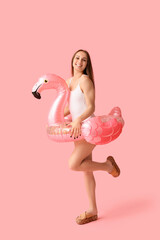 Beautiful young woman in stylish white swimsuit with inflatable ring in shape of flamingo on pink...