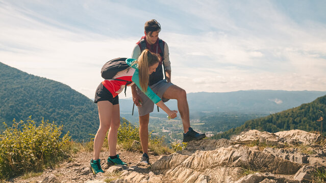 Smiling young man and a girl on a summer hiking trip, applying protection spray, a tick and mosquito repellent, with beautiful mountain scenery in the background
