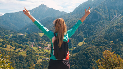 Cheerful girl hiker celebrating her success with raised outstretched arms, enjoying mountain...