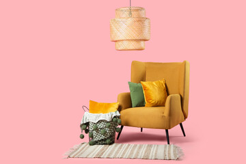 Comfortable armchair with pillows and  basket with cushion and plaid on pink background
