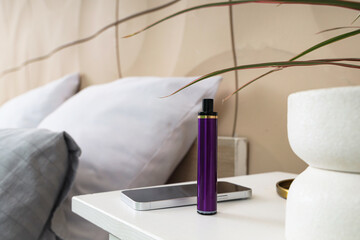 Purple disposable electronic cigarette and mobile phone on bedside table in room