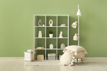 Shelving unit with decoration, lamp and pouf with pillows near green wall