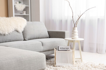 Interior of stylish living room with grey sofa, vase of willow branches on coffee table and...