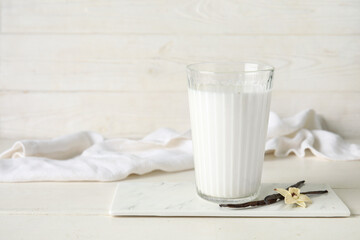 Glass of fresh vanilla milk with sticks and flower on white wooden background
