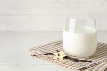 Glass of fresh vanilla milk with sticks and flower on white wooden background