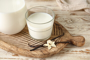Glass and jug of fresh vanilla milk with sticks and flower on white wooden background