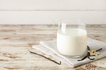 Glass of fresh vanilla milk with sticks and flower on white wooden background