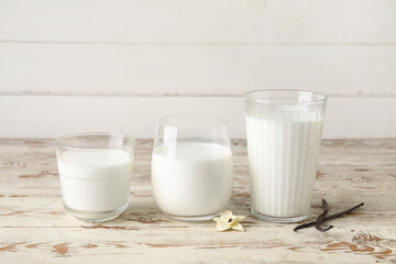 Glasses of fresh vanilla milk with sticks and flower on white wooden background