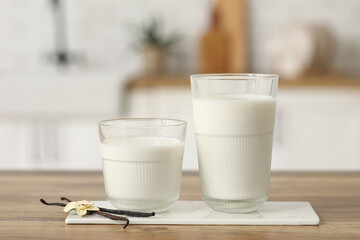 Glasses of fresh vanilla milk with sticks and flower on wooden table in kitchen