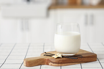 Glass of fresh vanilla milk with sticks and flower on white tile table in kitchen