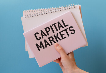 CAPITAL MARKETS text on a paper in hand with keyboard on blue background