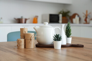 Teapot with plants and candles on dining table in kitchen, closeup