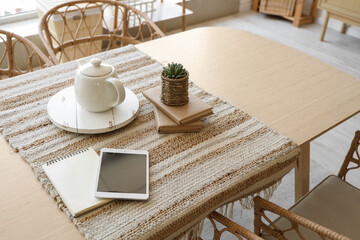 Teapot with tablet computer and books on dining table in room