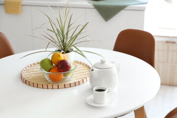 Teapot with cup of coffee and fruits on dining table in kitchen, closeup
