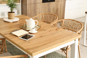 Teapot with notebooks and tablet computer on dining table in kitchen