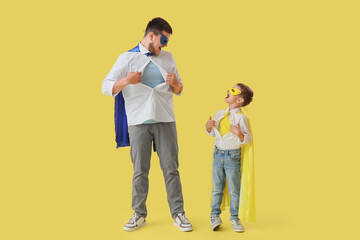 Little boy with his father in superhero costumes tearing their shirts on yellow background