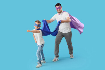 Little boy with his father in superhero costumes on blue background