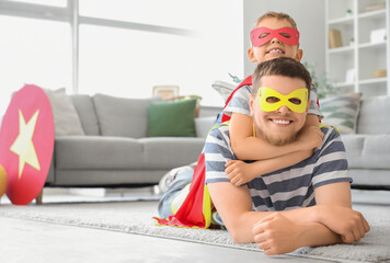 Little boy with his father in superhero costumes lying on floor at home