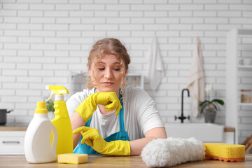 Female janitor with cleaning supplies on table in kitchen
